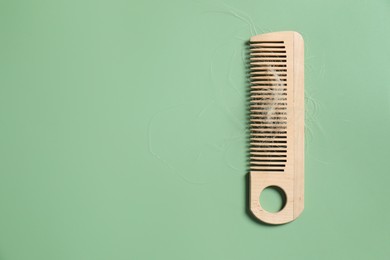 Photo of Wooden comb with lost hair on green background, top view. Space for text