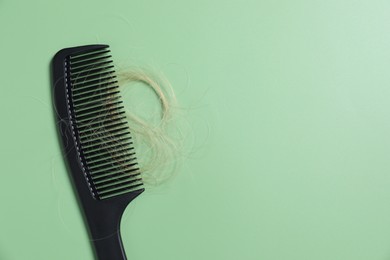 Photo of Comb with lost hair on green background, top view. Space for text