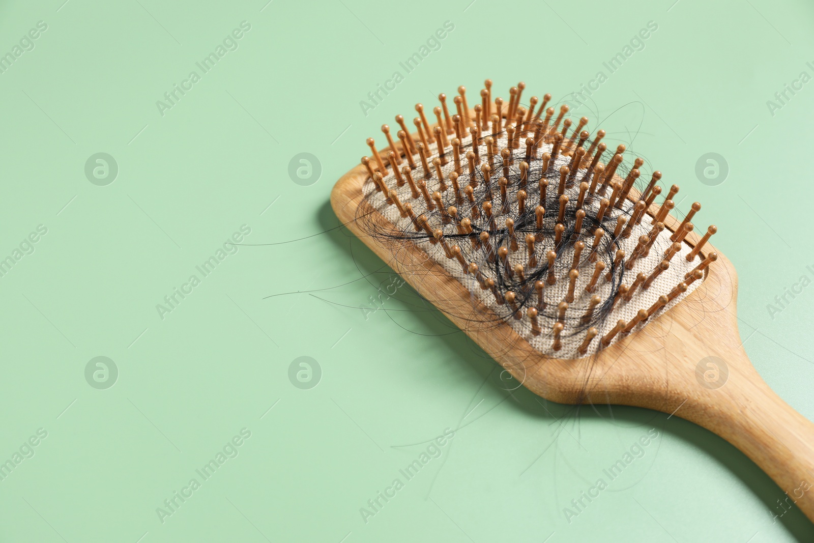 Photo of Wooden brush with lost hair on green background, space for text