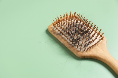 Wooden brush with lost hair on green background, space for text