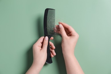 Woman taking her lost hair from comb on green background, top view