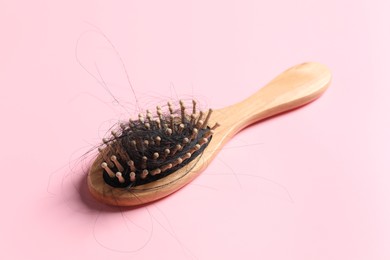 Photo of Wooden brush with lost hair on pink background