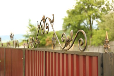 Photo of Metal fence with decorative wrought iron elements outdoors, selective focus