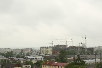 Picturesque view of city with buildings and construction cranes on cloudy day