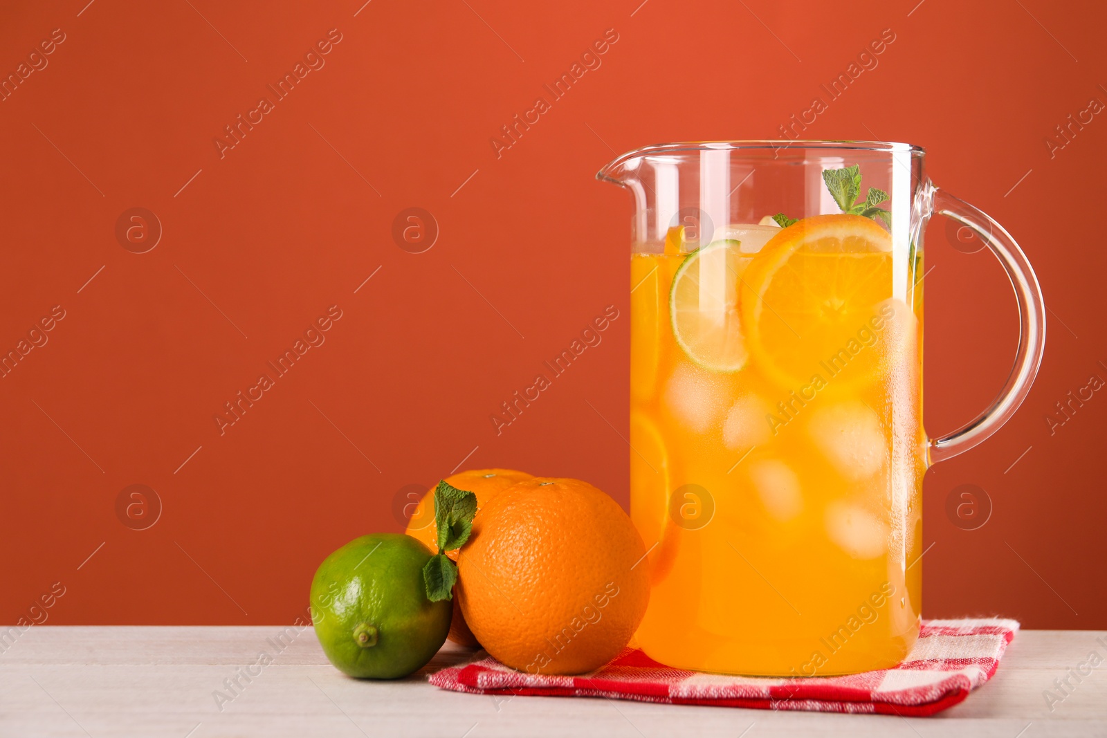 Photo of Freshly made lemonade in jug and citrus fruits on light wooden table, space for text