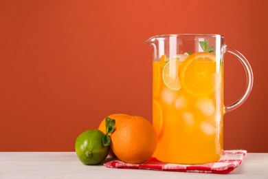 Freshly made lemonade in jug and citrus fruits on light wooden table, space for text