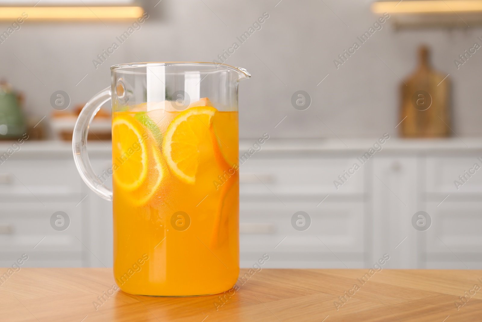 Photo of Freshly made lemonade in jug on wooden table in kitchen, space for text