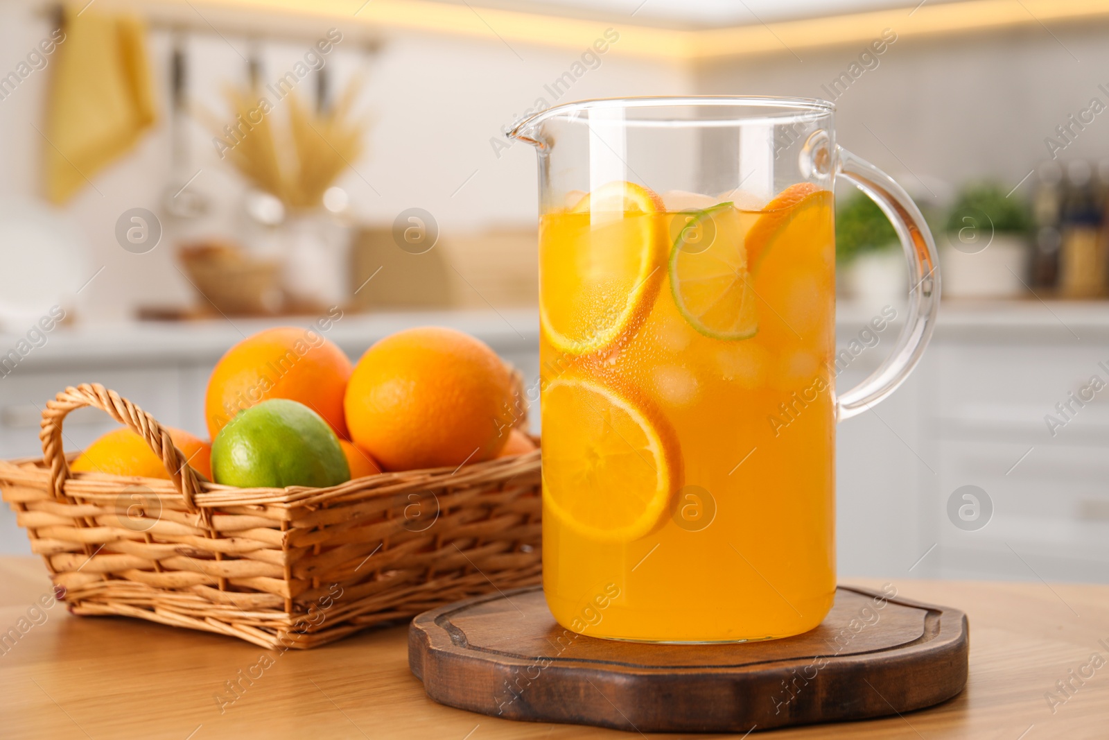 Photo of Freshly made lemonade in jug and citrus fruits on wooden table in kitchen