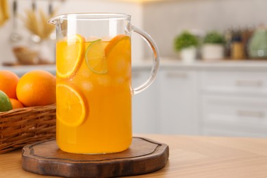 Photo of Freshly made lemonade in jug and citrus fruits on wooden table in kitchen, space for text