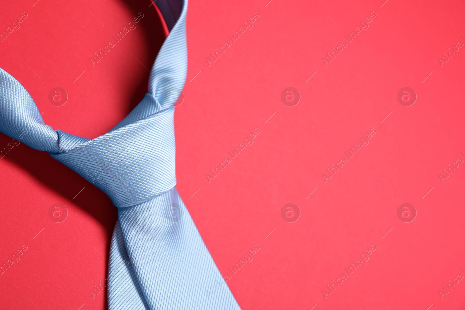 Photo of Light blue necktie on red background, closeup. Space for text