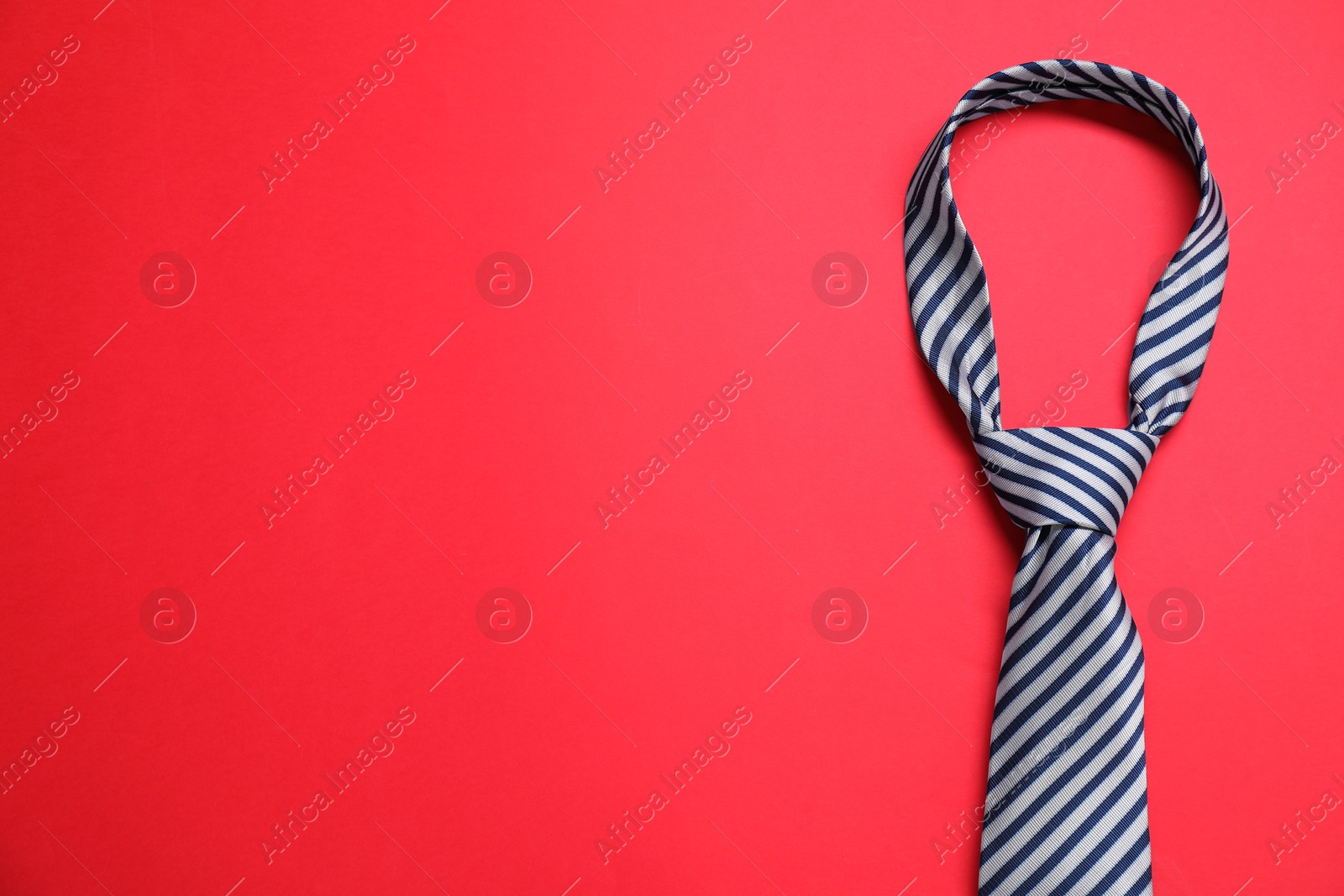 Photo of Striped necktie on red background, top view. Space for text