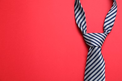 Striped necktie on red background, top view. Space for text