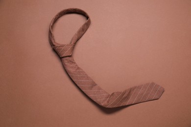 Photo of One striped necktie on brown background, top view