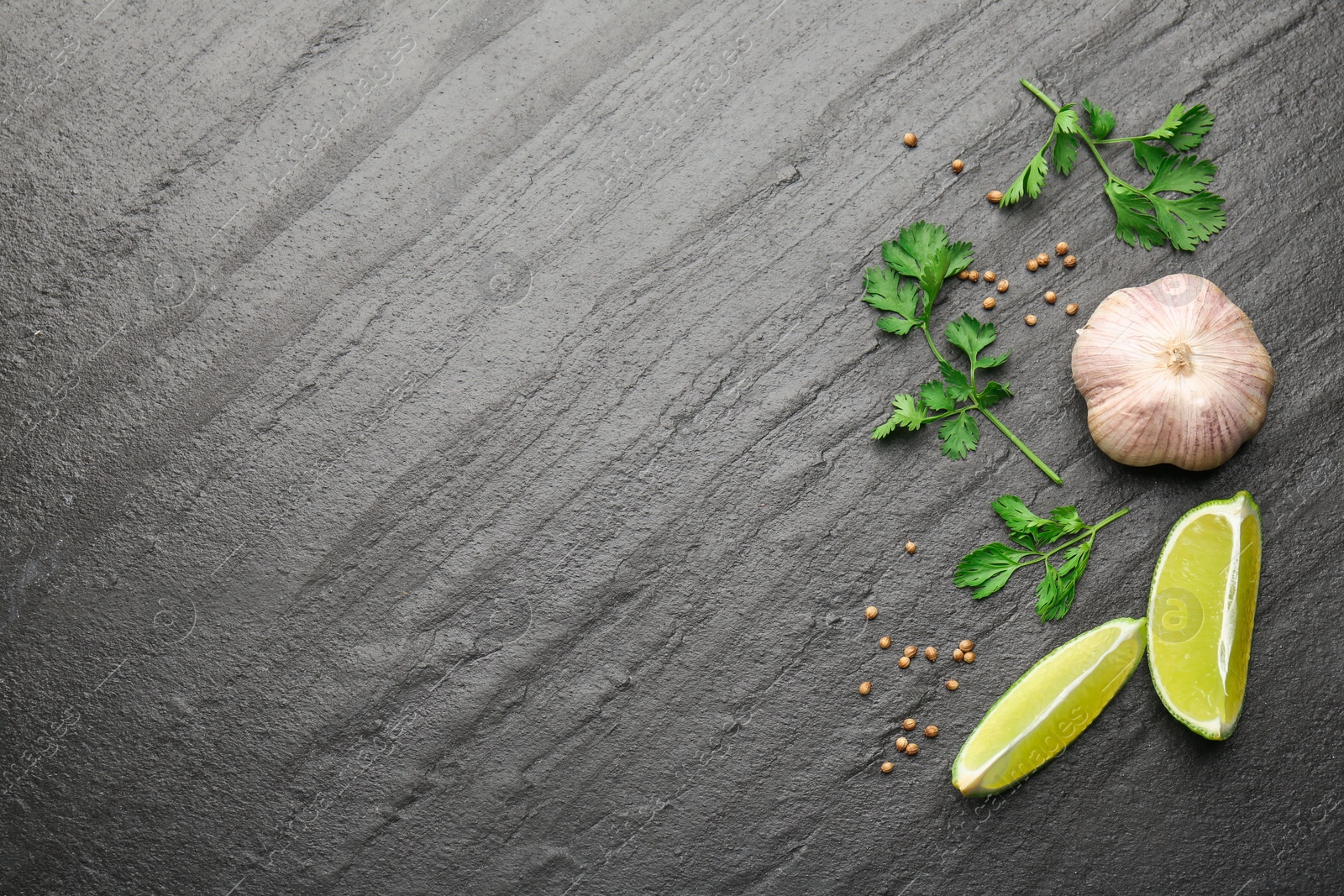 Photo of Fresh coriander leaves, dried seeds, garlic and lime wedges on black textured table, flat lay. Space for text