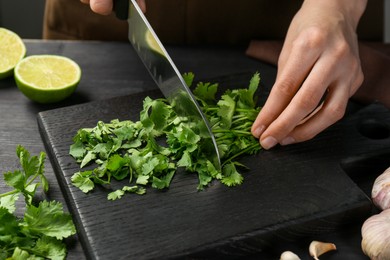 Photo of Woman cutting fresh coriander at black wooden table, closeup