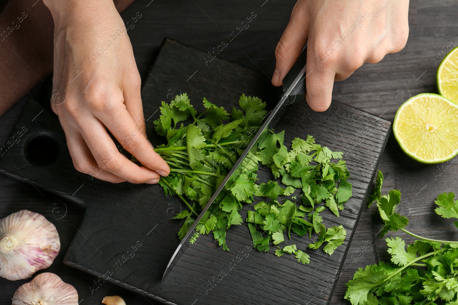 Photo of Woman cutting fresh coriander at black wooden table, above view