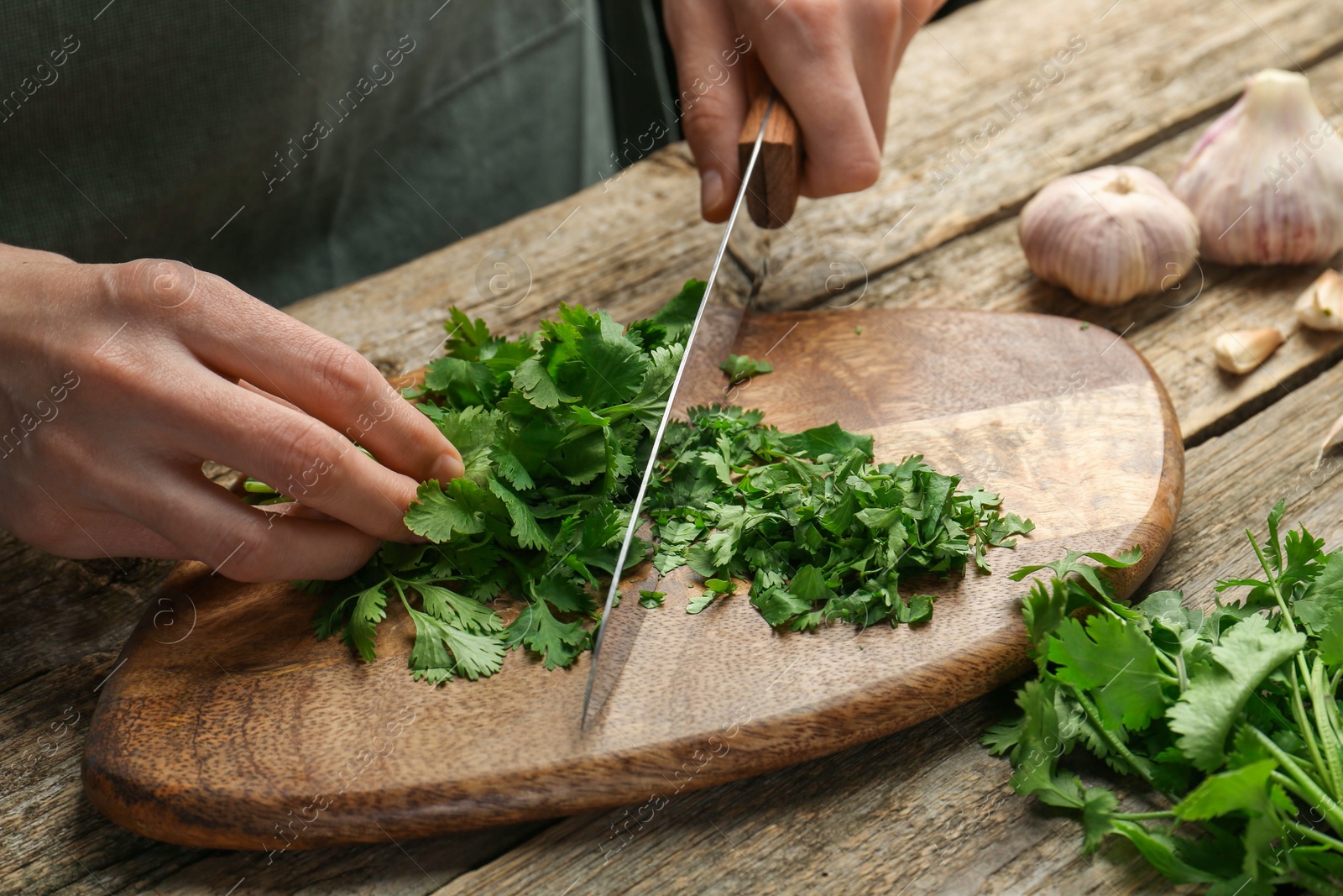 Photo of Woman cutting fresh coriander at wooden table, closeup