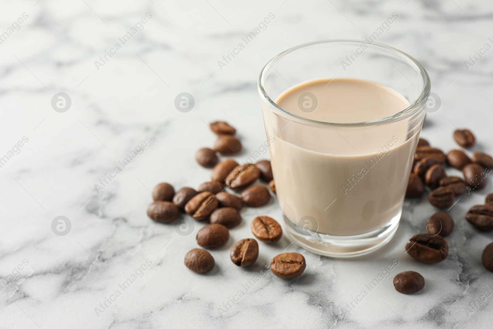 Photo of Coffee cream liqueur in glass and beans on white marble table, space for text