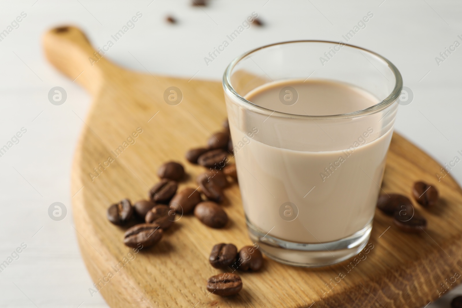 Photo of Coffee cream liqueur in glass and beans on white table, closeup
