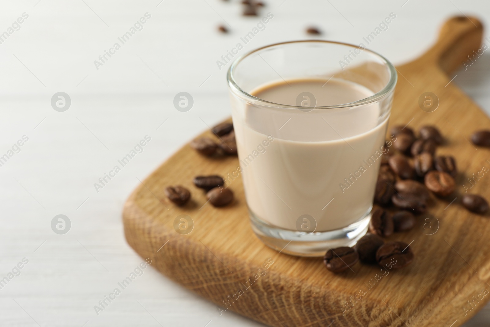 Photo of Coffee cream liqueur in glass and beans on white wooden table, closeup. Space for text