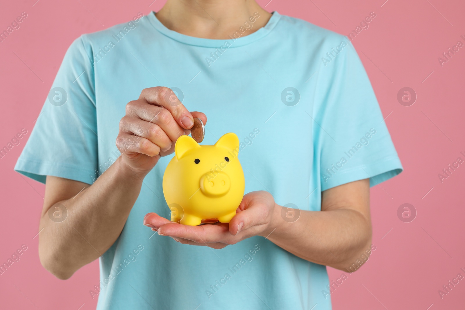 Photo of Woman putting coin into yellow piggy bank on pink background, closeup