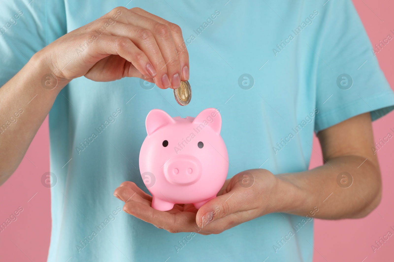 Photo of Woman putting coin into piggy bank on pink background, closeup