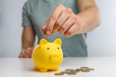 Photo of Man putting coin into yellow piggy bank at white table, closeup