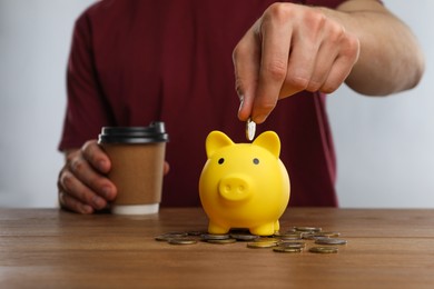 Man putting coin into yellow piggy bank at wooden table, closeup