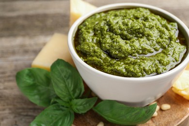 Photo of Tasty pesto sauce in bowl, basil, cheese and pine nuts on wooden table, closeup