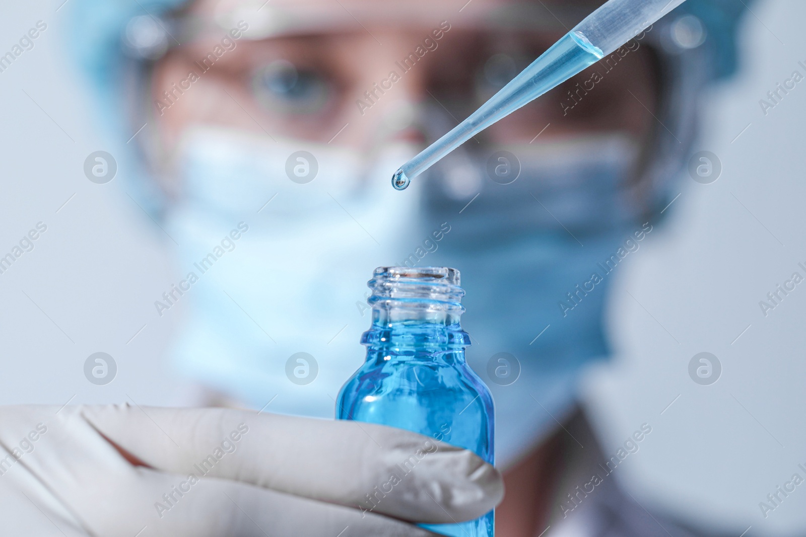 Photo of Scientist dripping liquid from pipette into glass bottle on light background, closeup