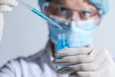 Photo of Scientist dripping liquid from pipette into glass bottle on light background, closeup