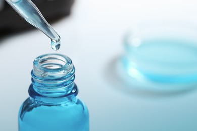Photo of Dripping liquid from pipette into glass bottle on blurred background, closeup. Space for text