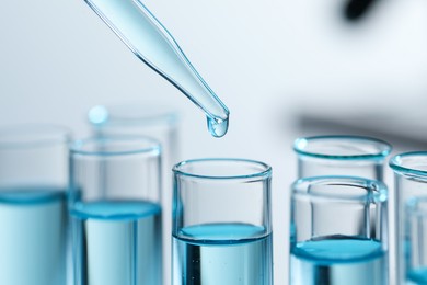 Dripping liquid from pipette into test tube on blurred background, closeup