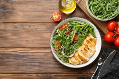 Photo of Healthy meal. Tasty salad and chicken breast in bowl and cutlery on wooden table, flat lay. Space for text