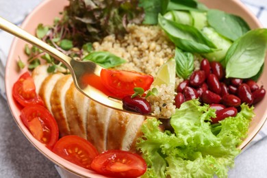 Healthy meal. Eating tasty vegetables, quinoa and chicken breast with fork from bowl on white table, closeup