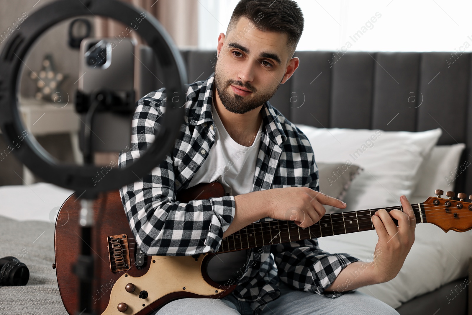 Photo of Music blogger recording guitar lesson with smartphone and ring lamp at home