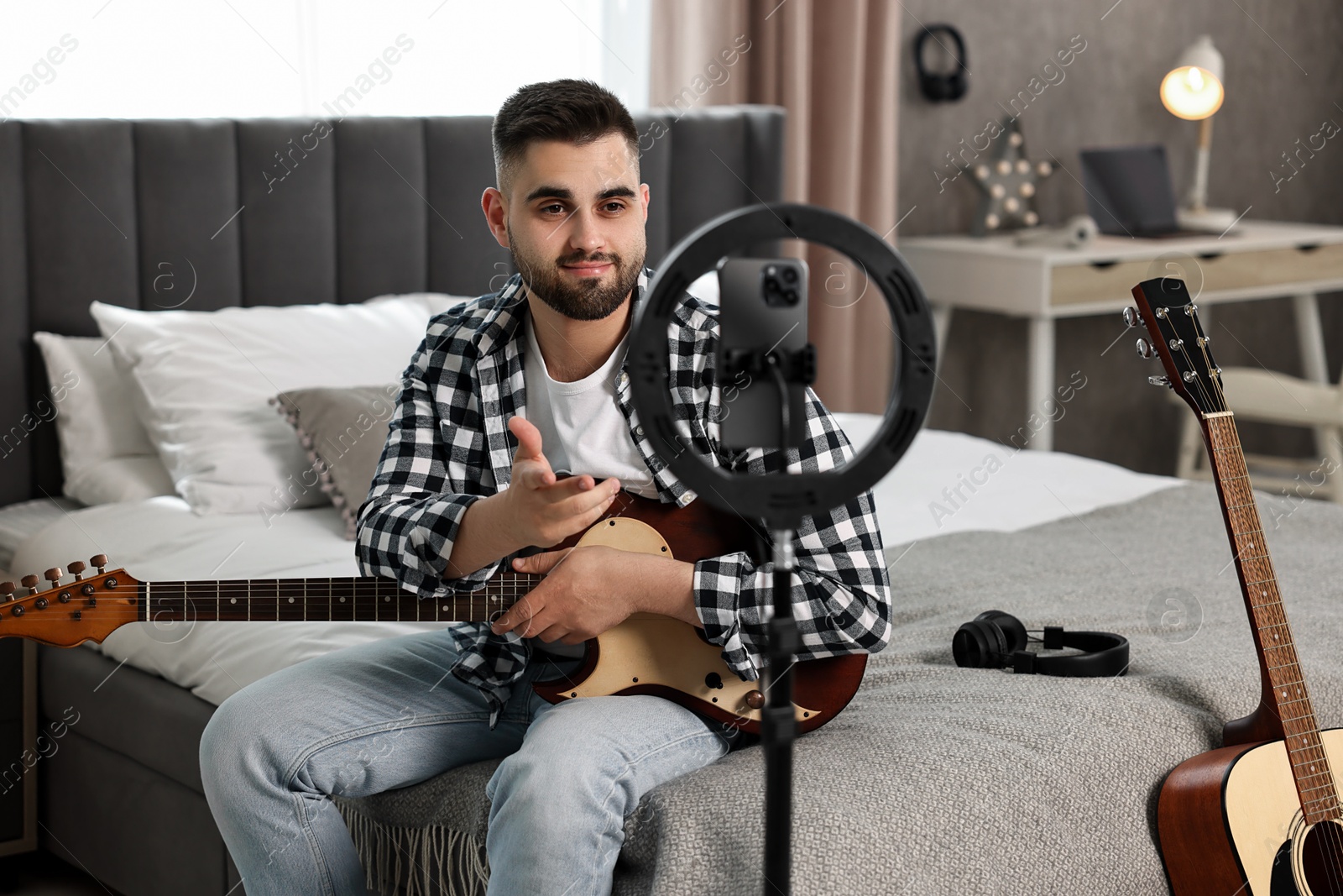 Photo of Music blogger recording guitar lesson with smartphone and ring lamp at home