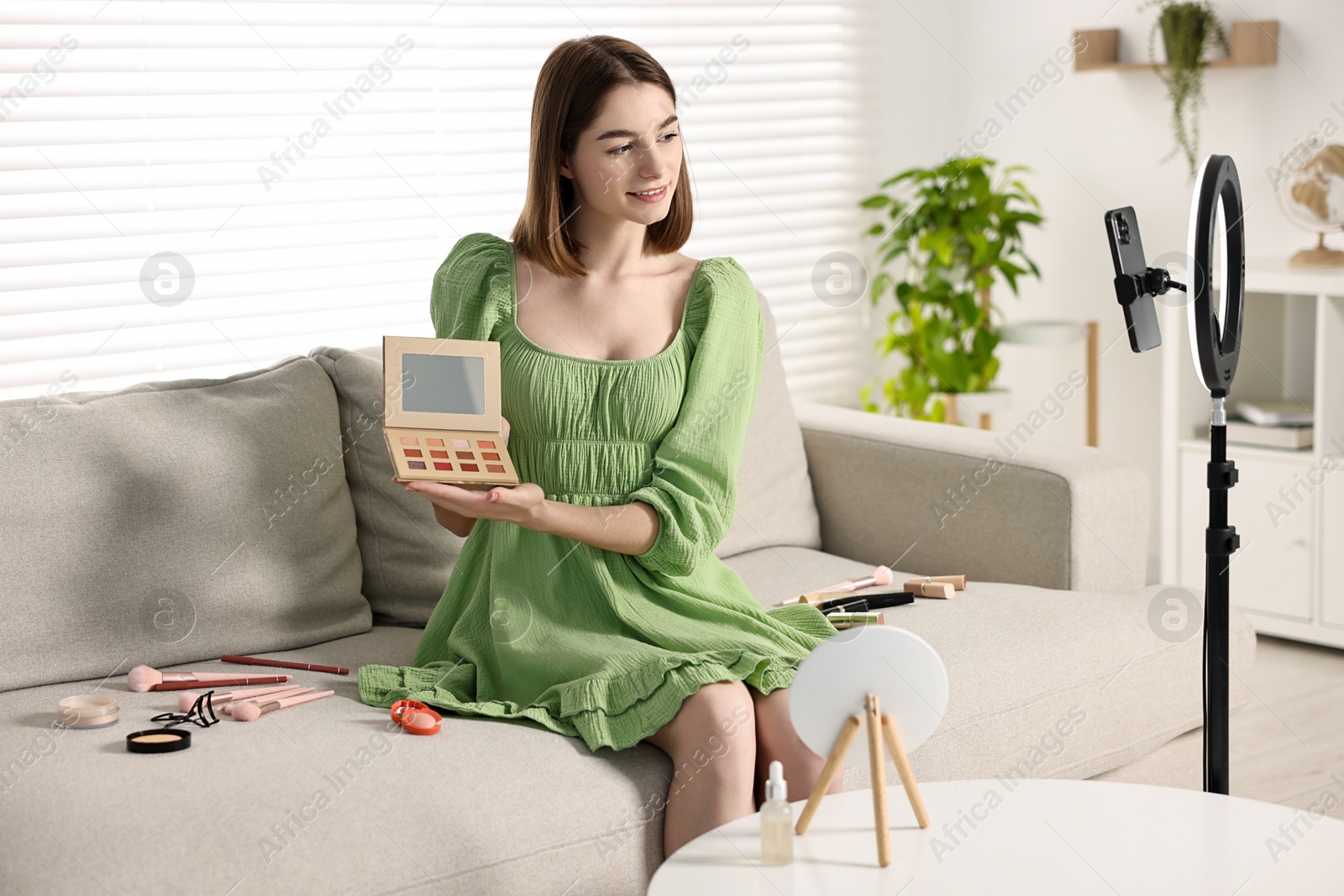 Photo of Beauty blogger reviewing eyeshadows and recording video with smartphone and ring lamp at home