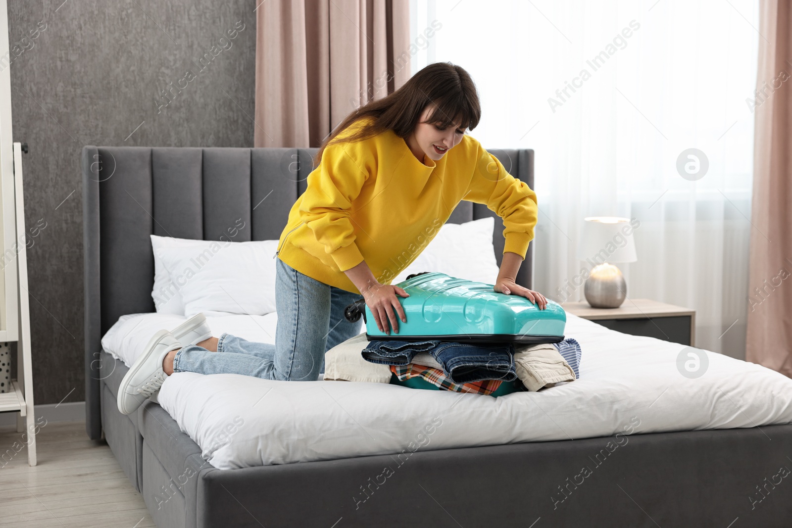 Photo of Woman packing suitcase for trip on bed indoors