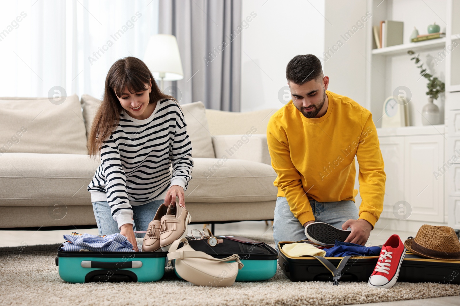 Photo of Couple packing suitcases for trip on floor at home