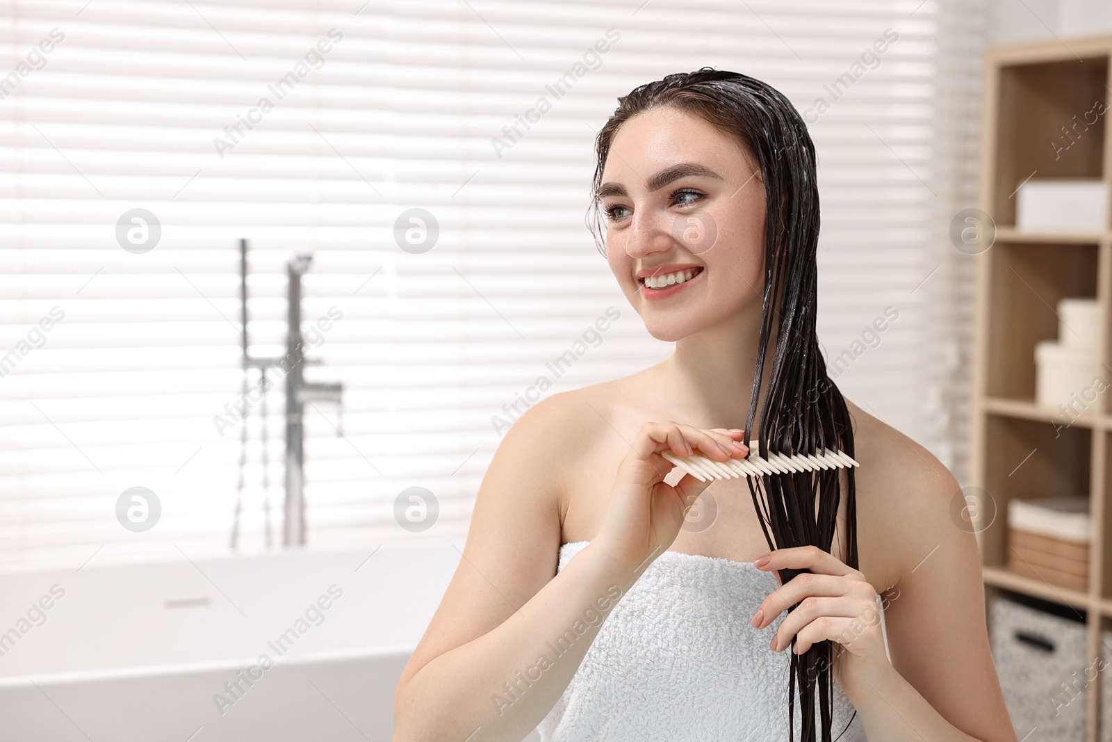 Photo of Smiling woman combing her hair with applied mask in bathroom. Space for text