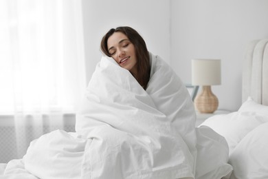 Happy woman wrapping in blanket sitting on bed. Good morning