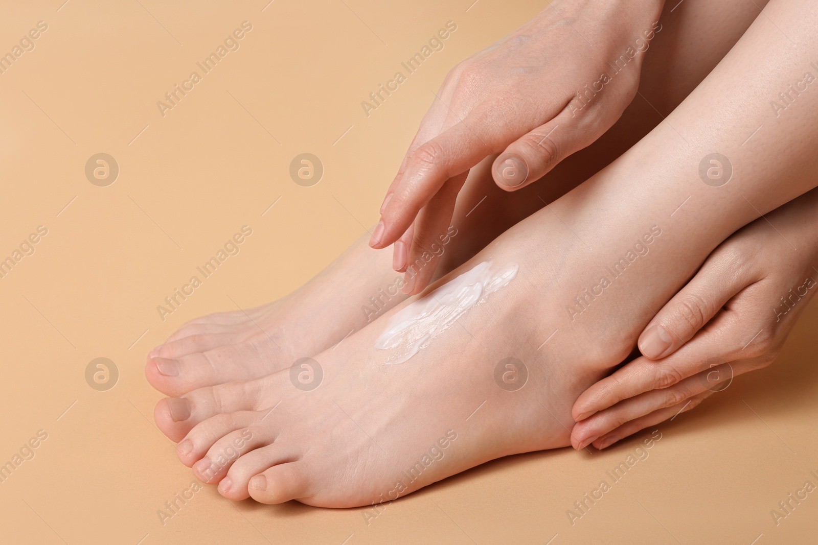 Photo of Woman applying moisturizing cream onto her feet on beige background, closeup. Body care