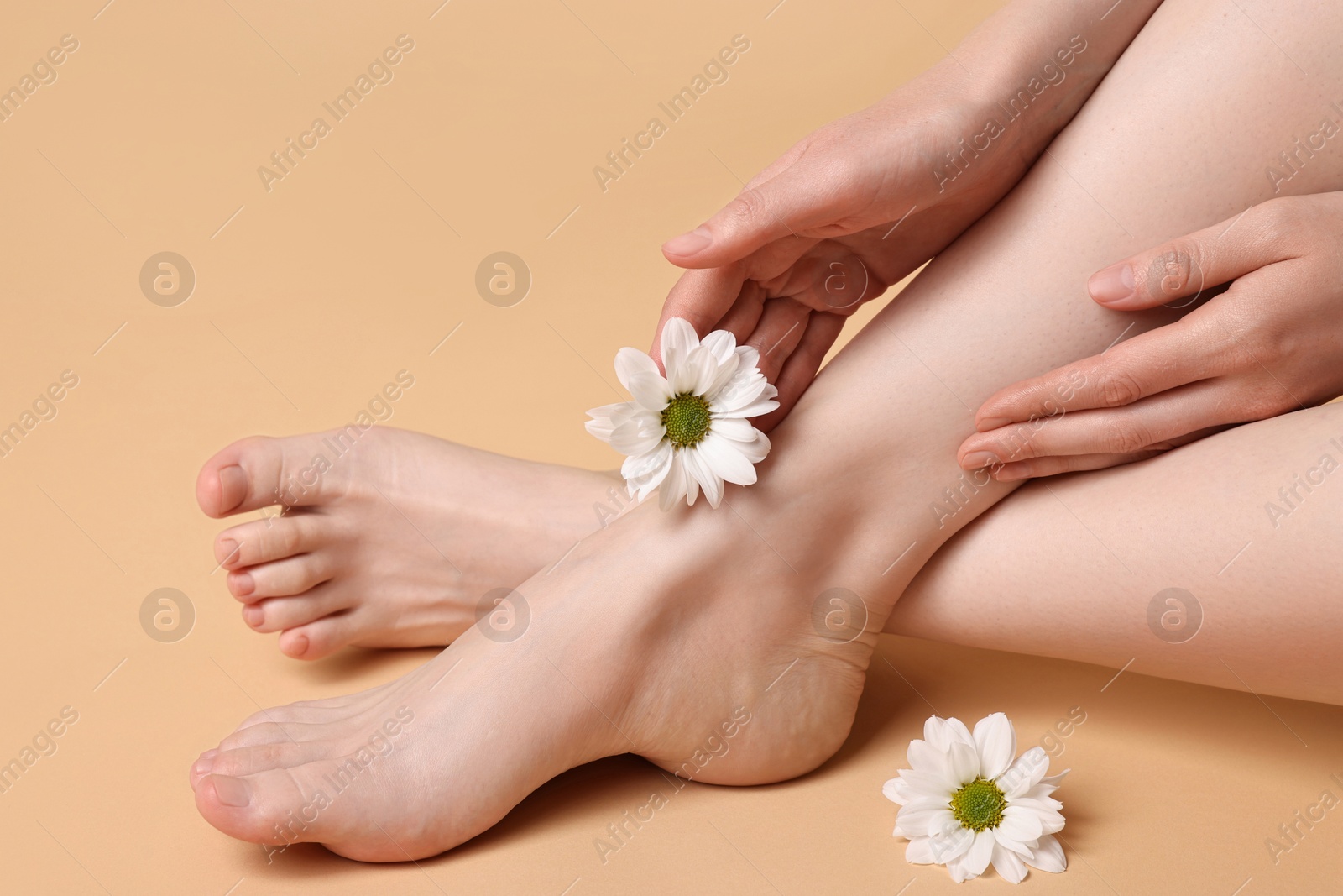 Photo of Closeup view of woman`s groomed feet after care procedure and beautiful flowers on beige background