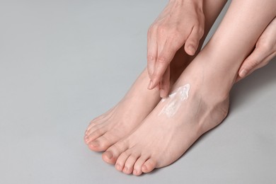 Photo of Woman applying moisturizing cream onto her feet on grey background, closeup. Body care