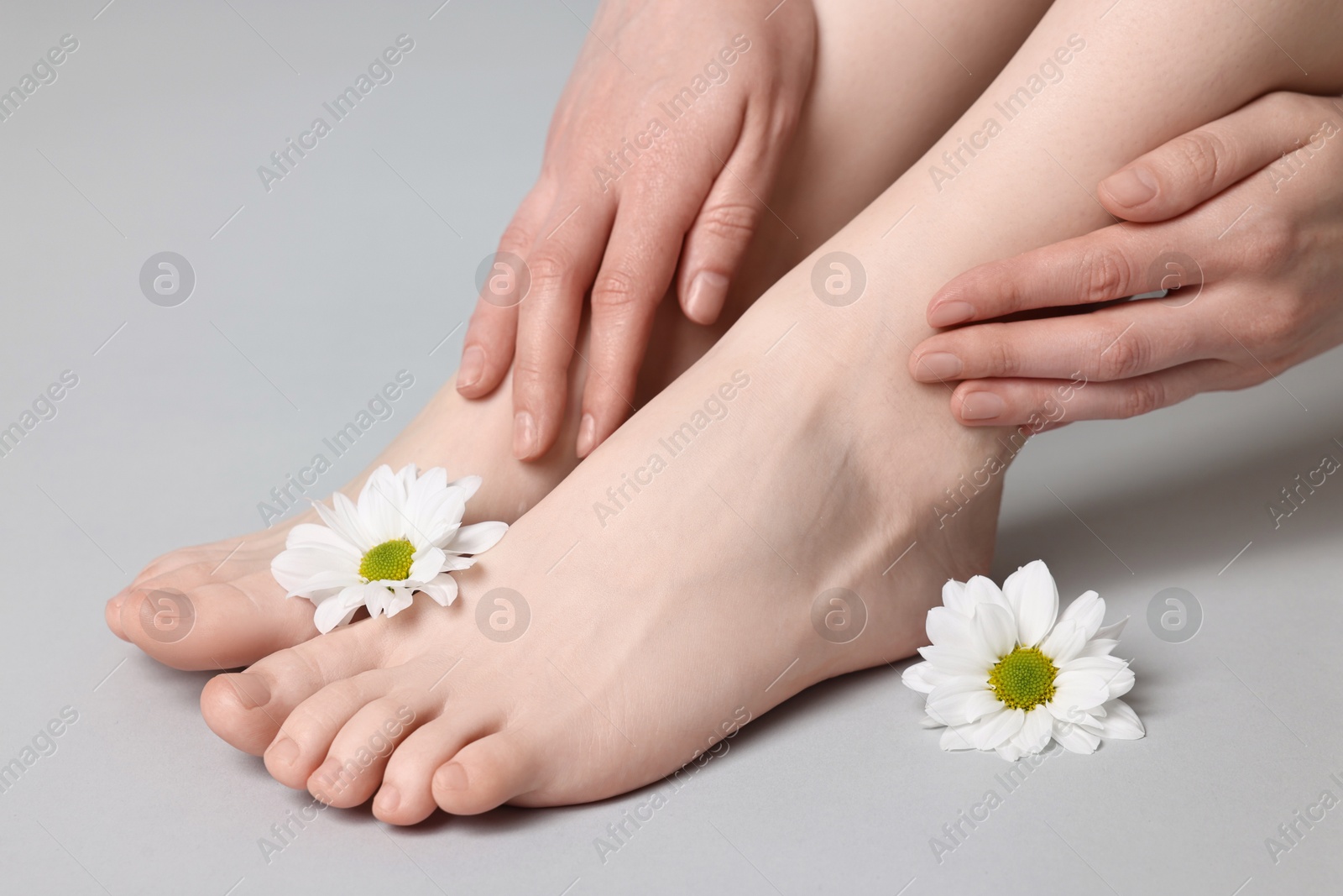 Photo of Closeup view of woman`s groomed feet after care procedure and beautiful flowers on grey background