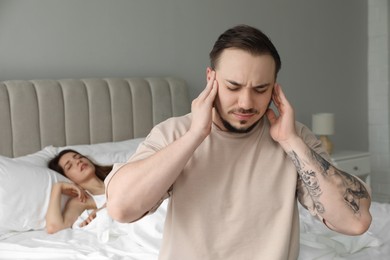 Photo of Bedtime. Irritated man covering ears near his snoring wife in bed at home