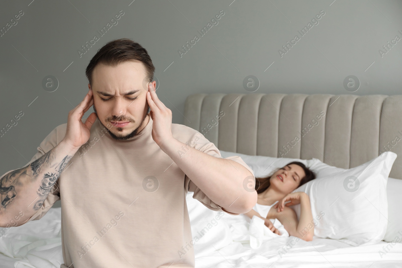 Photo of Bedtime. Irritated man covering ears near his snoring wife in bed at home