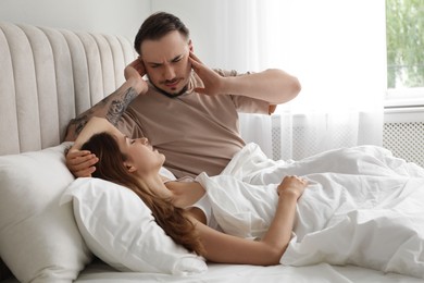 Bedtime. Irritated man covering ears near his snoring wife in bed at home