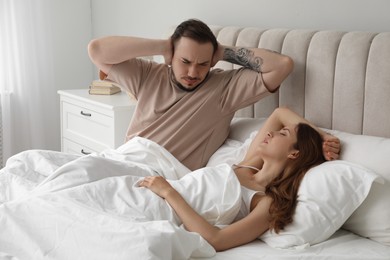 Bedtime. Irritated man covering ears near his snoring wife in bed at home